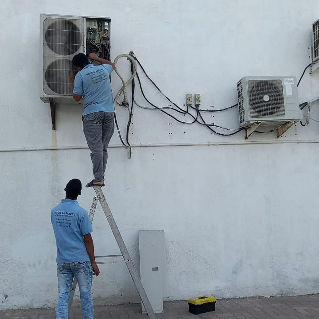 Two Noor Al Fareej technicians working on outdoor AC condenser wiring in Sharjah